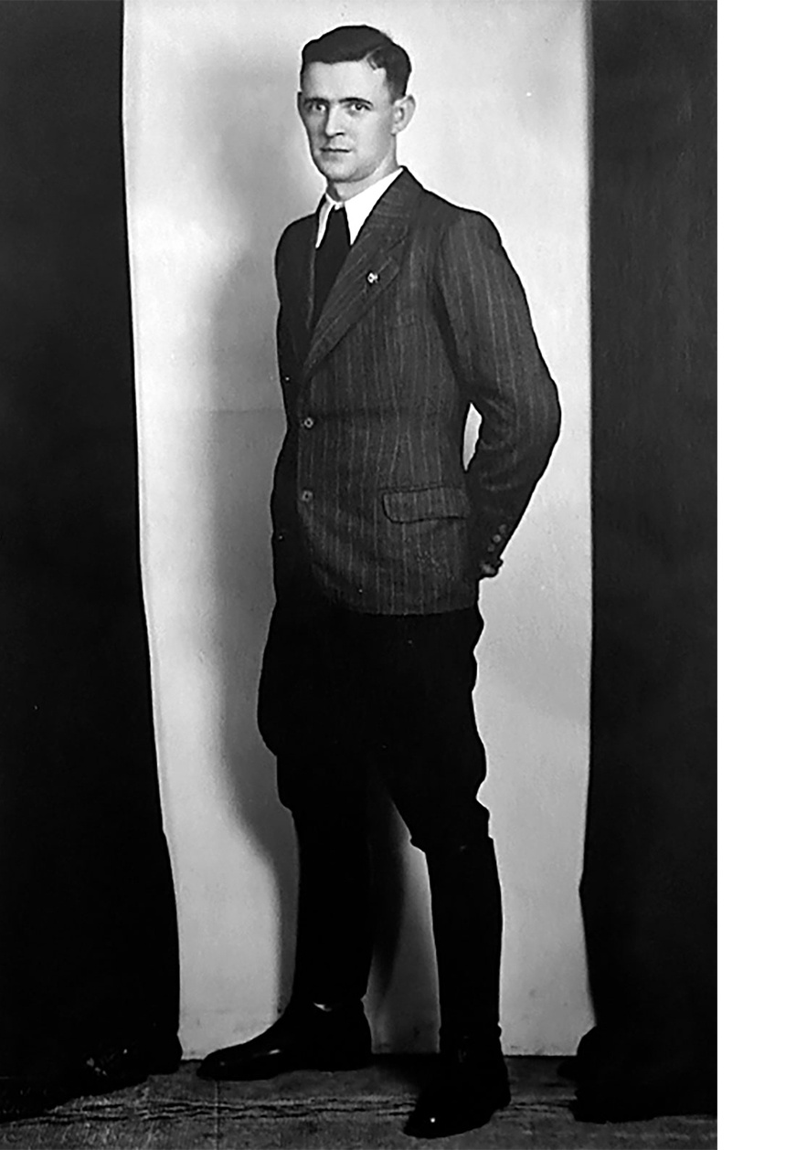 Totale, halb seitlich  von Mann mit kariertem Anzug, wei&szlig;em Hemd, dunkler Krawatte und Hakenkreuz Pinnadel am Revers, Lederstiefel. Blickt links an der Kamera vorbei. &copy; Deutsches Bundesarchiv