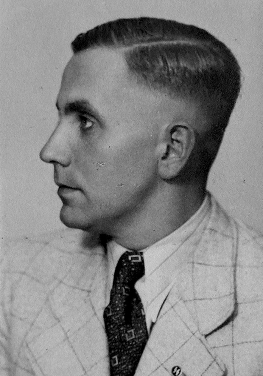 Halbprofil von Mann in hellem, kartierten Anzug, wei&szlig;em, leicht gestreiftem Hemd, gemusterter Krawatte und SS-Pinnadel am Revers. Blick nach Links von der Kamera aus. &copy; Deutsches Bundesarchiv