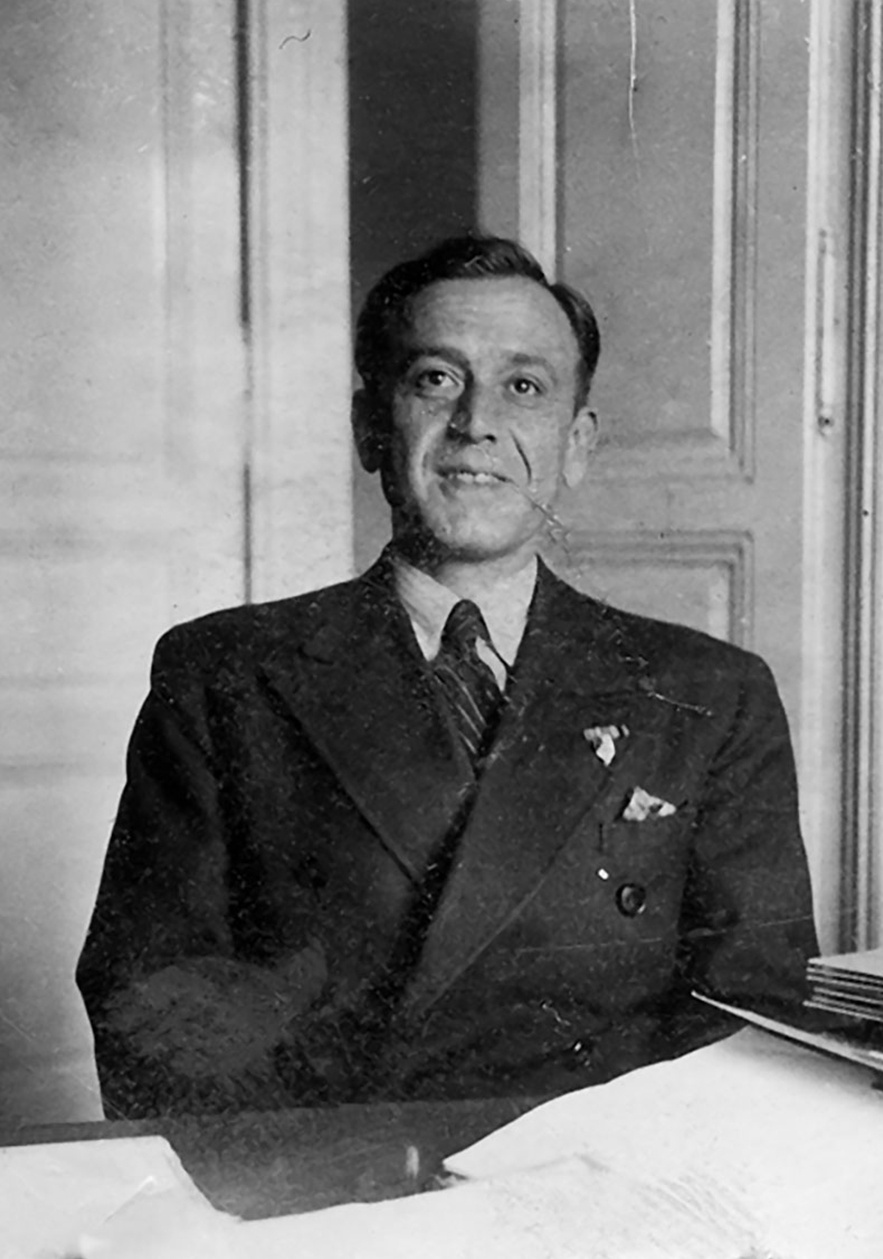 Mann mit Anzug, doppelreihige Konpfleiwte, Einstecktuch, nicht erkennbare Pinnadel am Revers, gestreifte Krawatte, helles, eventuell gestreiftes Hemd. Im HIntergrund eine offene, hell lackierte Holzt&uuml;r. &copy; &Ouml;StA / StiKo, Zl. 19 PA Blau