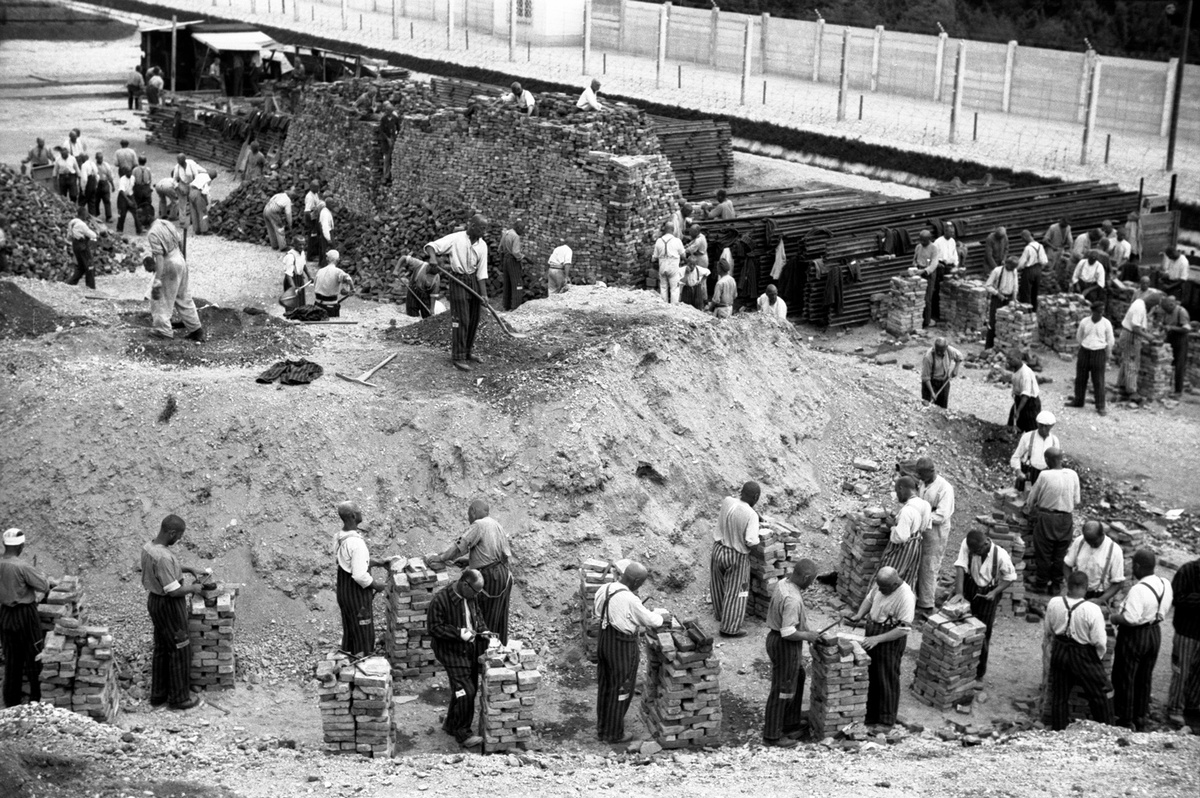 M&auml;nner stehen vor einem Schotterhaufen und schlichten Ziegelsteine aufeinander. Am H&uuml;gel arbeiten M&auml;nner mit Schaufeln und Hacken. Im Hintergrund weitere Arbeiter vor Ziegelsteint&uuml;rmen. &copy; Bundesarchiv / Friedrich Franz Bauer