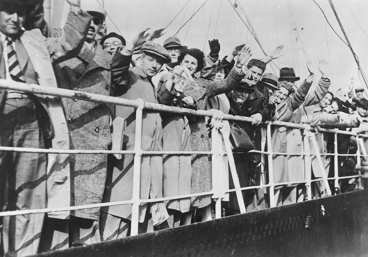 M&auml;nner und Frauen mit M&auml;nteln und teils H&uuml;ten stehen an der Reling eines Schiffes und heben die Hand zum Gru&szlig;. &copy; Bundesarchiv