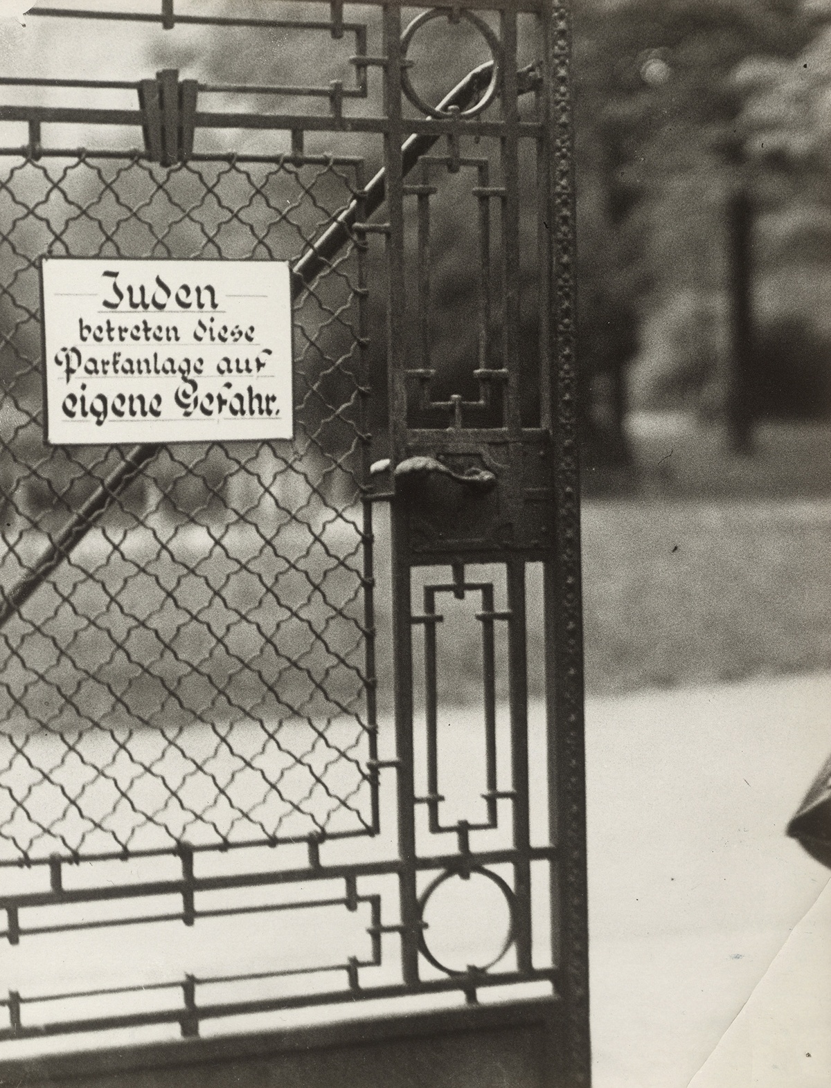 Gittertor, auf dem ein Schild mit der Aufschrift &bdquo;Juden betreten diese Parkanlage auf eigene Gefahr&ldquo; angebracht ist. Im Hintergrund ein Gehweg, Wiese und B&auml;ume. &copy; &Ouml;NB Bildarchiv