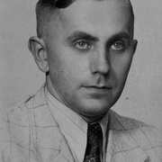 Halbprofil von Mann in hellem, kartierten Anzug, wei&szlig;em, leicht gestreiftem Hemd, gemusterter Krawatte und SS-Pinnadel am Revers. Blick rechts an der Kamera vorbei. &copy; Deutsches Bundesarchiv