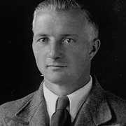 Frontalportrait eines Mannes mit kurzen vermutlich grauen Haaren, schmalgestreifter Anzug, wei&szlig;em Hemd, dunkler Krawatte, Hakenkreuz-Pinnadel am Revers. Blickt leicht links an der Kamera vorbei. &copy; Deutsches Bundesarchiv